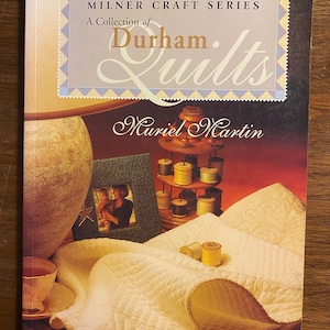 May include: A book titled "Durham Quilts: A Collection of Durham Quilts" by Muriel Martin. The cover features a white quilt with a heart-shaped design, spools of thread, and a vintage-style teacup and saucer.