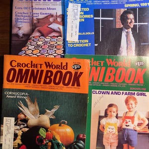 May include: Four vintage crochet pattern magazines with the title "Crochet World Omnibook" on the cover. The covers feature a variety of crochet projects, including a cornucopia, a clown and farm girl, Christmas ornaments, and dolls. The magazines are from the 1980s.