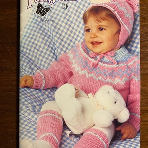 May include: A pink and blue knitted baby sweater and hat set with a white teddy bear. The pattern is a Fairytale DK by Patons. The pattern number is 488 and the price is $2.95.