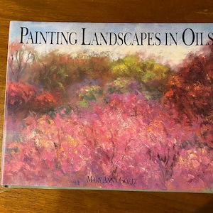 May include: Book cover with the title "Painting Landscapes in Oils" by Mary Anna Goetz. The cover features a colourful landscape painting of trees and foliage in shades of pink, green, red, and yellow.