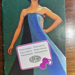 Puede incluir: Una mujer lleva un vestido a rayas azules y negras con una raya blanca. El vestido está hecho de tejido de punto. La imagen incluye el texto "Points fantaisie, Fancy patterns, Fantasiemuster, Punti fantasia, Puntos fantasia, Fantasiesteekken, SUPERBA".
