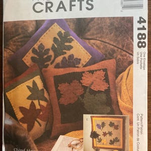 以下が含まれることがあります： McCall's Crafts 4188の裁縫型紙封筒。オレンジ、黄色、緑、紫、茶色の布製リーフアップリケで装飾された正方形のクッションとテーブルランナーのイラストが描かれており、デザイナー名Cheryl Haynesが記載されています。