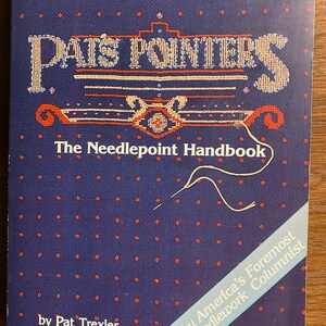 Op de afbeelding: Een blauw boek met de titel "Pats Pointers The Needlepoint Handbook" door Pat Trexler, door America's Foremost Needlework Columnist.