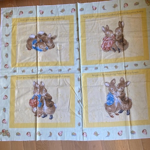 May include: Fabric panel featuring four illustrated scenes of Peter Rabbit and Benjamin Bunny. The scenes include text captions and are set against a light yellow background with a border of leaves and berries. The illustrations depict the characters in various poses.