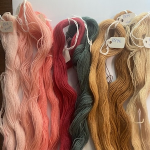 May include: A collection of six skeins of yarn in varying colors including light pink, coral, deep red, dark forest green, mustard yellow, and beige. Each skein features a small white paper tag with handwritten numbers such as 8818, 8846, and 8845.