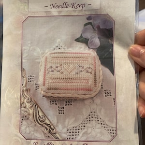 Puede incluir: Un kit de manualidades etiquetado como "Sarah Belle Needle-Keep" de Lorri Birmingham Designs. El kit incluye un estuche para agujas de punto de cruz con un diseño beige y rosa. El tamaño final es de aproximadamente 5,7 cm de largo por 3,8 cm de ancho.