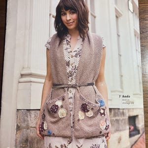 May include: A woman wearing a beige knitted vest with two large pockets adorned with fabric embellishments. The vest is belted at the waist. The image includes the text "Vintage DK & Vintage" and "1 kado knit in Vintage DK".