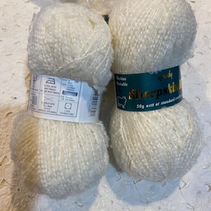 May include: Two off-white yarn skeins with labels. One label reads "COOL IRON DRY PRESS" and "APPROX. 135 meters". The other label reads "Machine Washable" and "Sheepskin". The yarn is a soft, textured material, suitable for knitting or crochet projects.