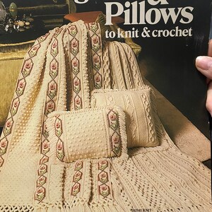 May include: A book titled "Afghans & Pillows to knit & crochet" with designs by Marion Graham. The cover features a close-up of a crocheted throw blanket and pillows in a cream colour with a delicate floral pattern.