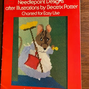 Op de afbeelding: Een vintage kruissteekpatroonboek met een rode kaft. De kaft toont een kruissteekillustratie van een muis met een bezem en een gele plumeau. Het boek heet "Needlepoint Designs after Illustrations by Beatrix Potter."