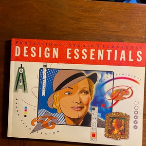 May include: A book titled "Professional Studio Techniques Design Essentials" featuring Adobe Photoshop and Illustrator. The cover features a colorful illustration of a woman with a hat, a compass, and a paint palette.