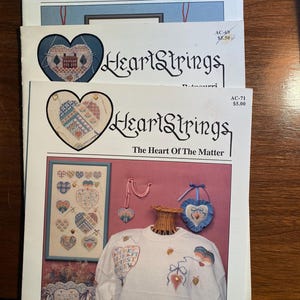 May include: Three HeartStrings cross stitch patterns featuring a variety of heart designs. The patterns are titled "A Homespun Holiday", "Bourri", and "The Heart Of The Matter".