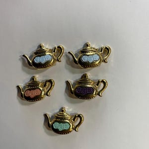 Puede incluir: Cinco encantos de tetera de oro con diseños florales de diferentes colores. Las teteras son pequeñas y tienen un diseño detallado.