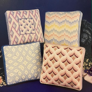 Puede incluir: Cuatro diseños de almohadas cuadradas de bargello. Las almohadas son en tonos de rosa, azul, amarillo y blanco. Los diseños son geométricos e intrincados. Las almohadas son todas del mismo tamaño y tienen un borde blanco.