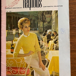 May include: A magazine cover featuring a woman wearing a yellow sweater and white skirt, sitting at an outdoor cafe. The magazine is titled "Reynolds" and features the text "Continental Collection" and "Designer Sweaters by Windsor Button Shop".