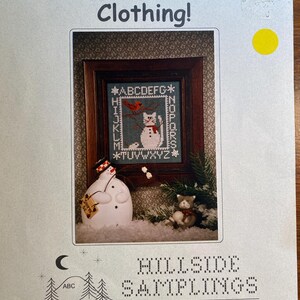 May include: Cross stitch pattern for a cat wearing a snowman's hat and scarf. The pattern includes the alphabet and numbers. The pattern is from Hillside Samplings, 1927 Lapham Rd., East Aurora, NY 14052 (716) 655-4091. Designs by Lesley Rudnicki.