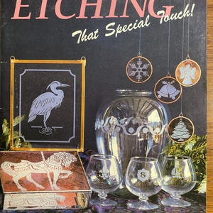 Puede incluir: Un libro titulado "Etching That Special Touch!" de Janet Schrader. La portada del libro presenta una variedad de objetos de vidrio grabado, incluyendo un jarrón, adornos y una caja. El libro es presentado por Carolyn Kyle.