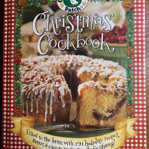 May include: A Christmas Cookbook with a red and white checked border. The cover shows a cake with white icing and nuts, and the text "Christmas Cookbook." A banner reads "Filled to the brim with 191 holiday recipes, menus & easy-to-make treats for sharing!"