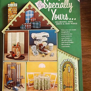 May include: A book cover with the title "Specially Yours... Decorating with Sheets & Mod Podge" and a picture of a house with different rooms decorated with fabric and Mod Podge. The book cover is green with a white border and the title is in a white font. The author's name is "Jan Meyerson Wetstone".