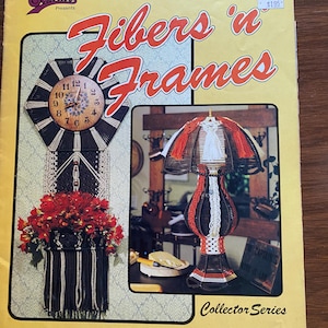 May include: A book cover for a craft project titled "Fibers 'n Frames" with a red, white, and black clock and a red, white, and black lampshade. The book cover is yellow with a brown border.