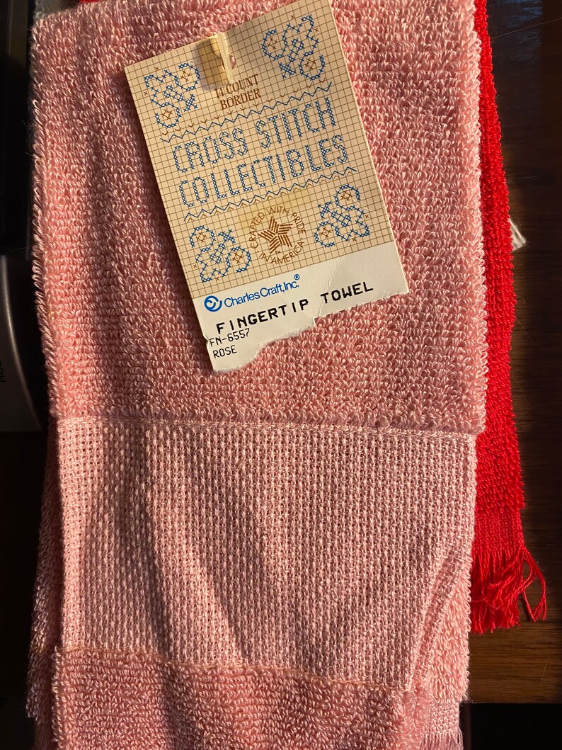 May include: A pink fingertip towel with a white label that says "Cross Stitch Collectibles" and "Charles Craft, Inc."  The label also says "Fingertip Towel" and "FN-6557 ROSE".