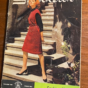 May include: A vintage magazine cover featuring a woman in a red knitted dress standing on a set of stairs. The magazine is called "Spinnerin" and the cover text reads "Fashion Magic".