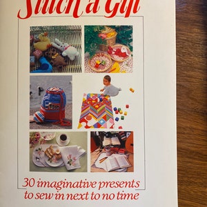 May include: Book cover with the title "Stitch a Gift" in red lettering. The cover features photos of handmade gifts, including a stuffed animal, a baby blanket, a backpack, and a knitted dishcloth. The text below the photos reads "30 imaginative presents to sew in next to no time."