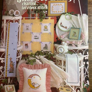 Peut inclure: Un livre de patrons de point de croix vintage intitulé "Just For Baby" par Leisure Arts. La couverture présente divers projets de point de croix sur le thème des bébés, dont un oreiller avec un motif de lune et d'étoiles et une annonce de naissance encadrée.