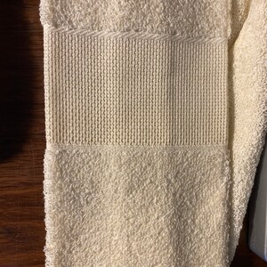 May include: A white towel with a textured pattern. The towel is folded in half and has a fringe on one end.