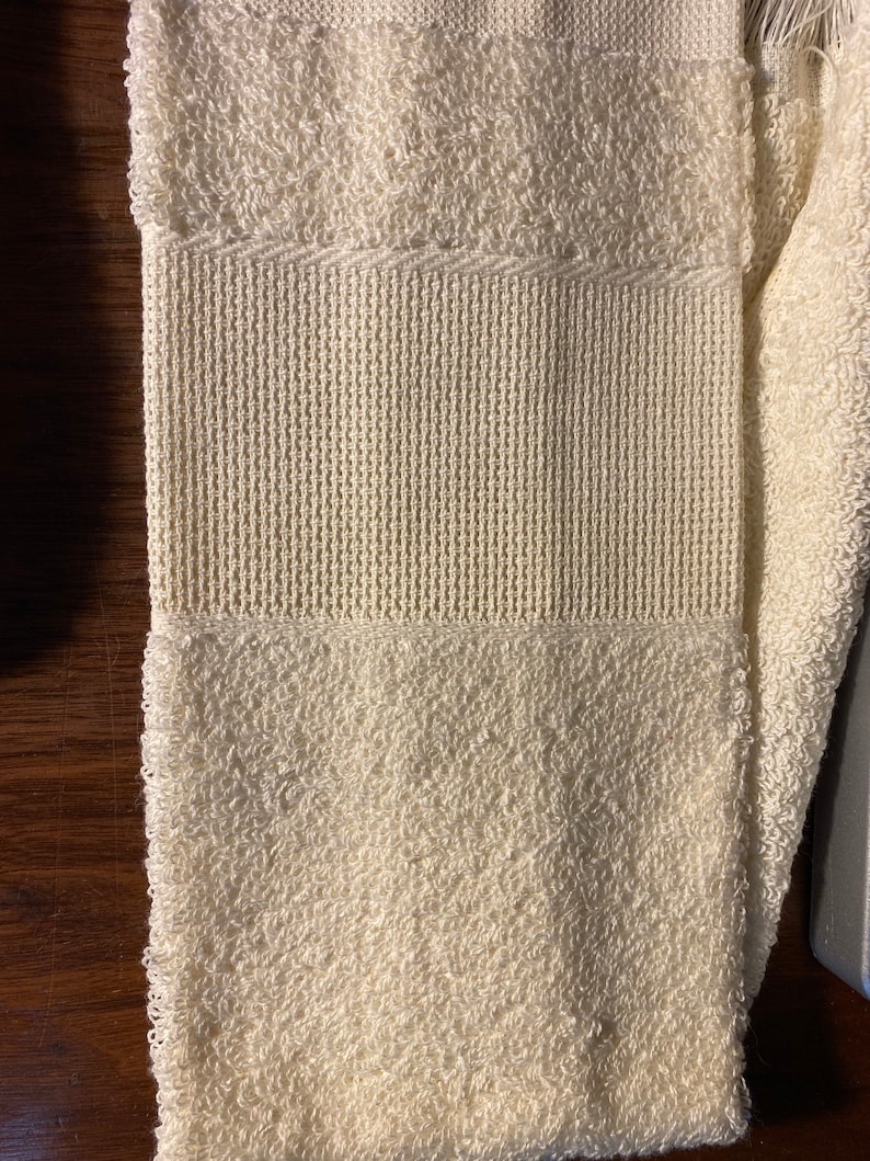 May include: A white towel with a textured pattern. The towel is folded in half and has a fringe on one end.