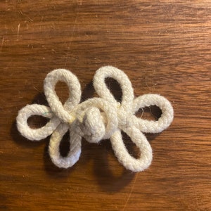 May include: A white rope tied in a decorative knot, resembling a flower, on a brown wooden surface.