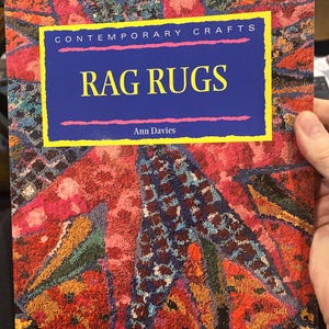 May include: A book cover titled "RAG RUGS" with the text "CONTEMPORARY CRAFTS" above it. The cover features a colorful, textured design in shades of red, orange, blue, and green. The author's name, Ann Davies, is at the bottom.