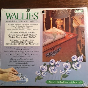 Puede incluir: Un paquete de pegatinas de pared de rosas azules. El paquete muestra un primer plano de las pegatinas en un cofre de madera. El texto en el paquete dice "Walllies Wallpaper Cutouts" y "¡Decora en minutos!"