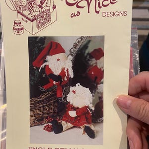 May include: A cream-colored paper with a Santa Claus doll pattern. The text reads "Twice as Nice Designs" and "Jingle Belly Santa." The pattern includes two Santa dolls, one standing and one sitting. The sizes are 6 or 8 inches.