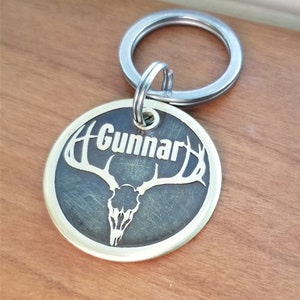 May include: Brass dog tag with a deer skull and antlers design. The tag is engraved with the name "Gunnar".