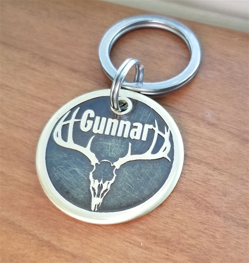 May include: Brass dog tag with a deer skull and antlers design. The tag is engraved with the name "Gunnar".