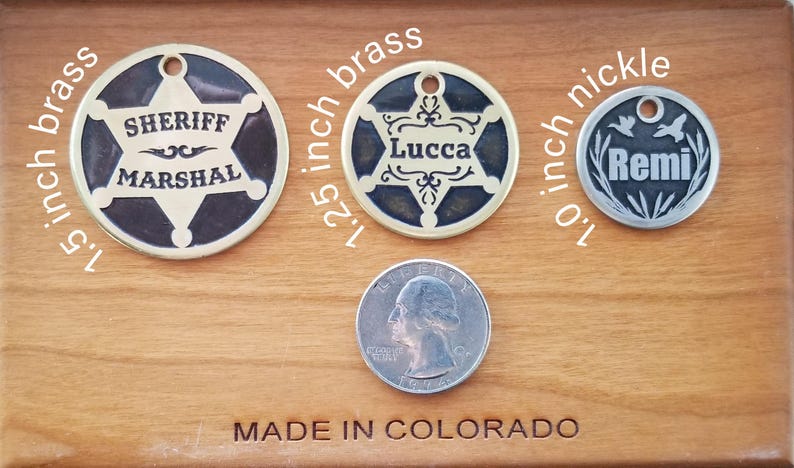 May include: Three circular metal pet tags with holes for attachment. The 1.5 inch brass tag features a sheriff star and the text SHERIFF MARSHAL. The 1.25 inch brass tag has a star and the name Lucca. The 1.0 inch nickel tag shows birds and the name Remi.