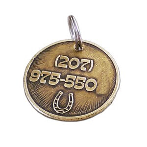 May include: Brass dog tag with a horseshoe design and the phone number (207) 975-550.