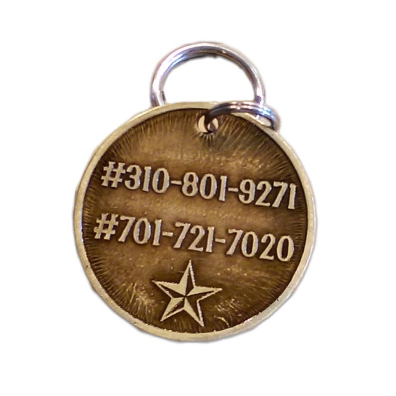 May include: A round, brass dog tag with a star engraved on the front. The tag has two phone numbers engraved on it: #310-801-9271 and #701-721-7020.
