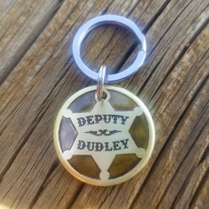 May include: A gold-toned keychain featuring a sheriff's star design. The star has the words "DEPUTY DUDLEY" inscribed on it.