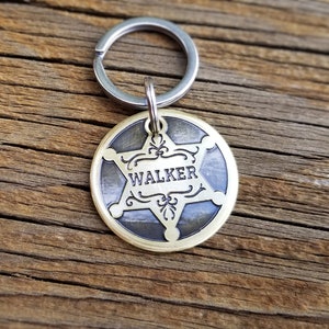 May include: A brass dog tag with a five-pointed star design and the name "WALKER" engraved on it. The tag is attached to a silver key ring.