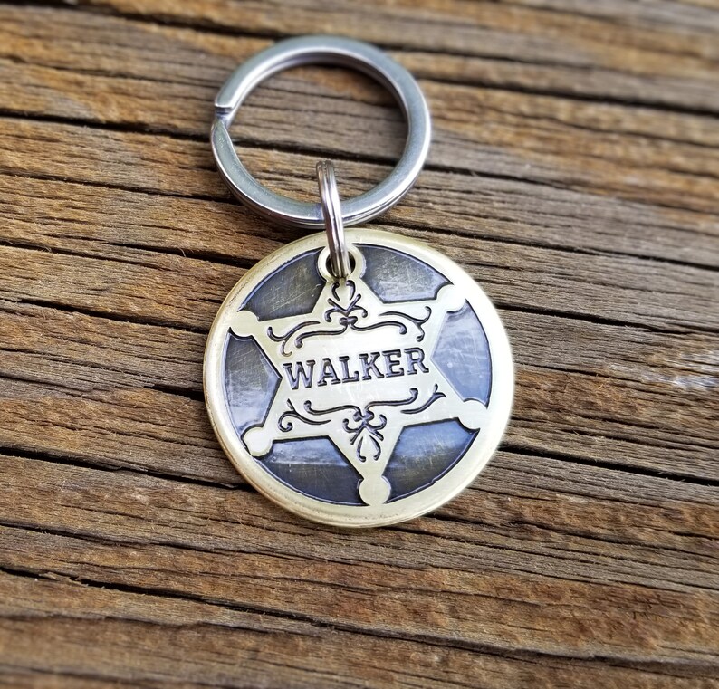 May include: A brass dog tag with a five-pointed star design and the name "WALKER" engraved on it. The tag is attached to a silver key ring.