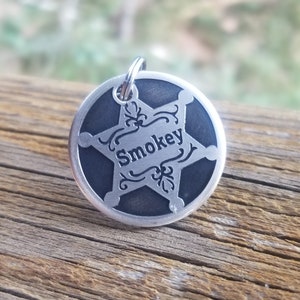 May include: A silver metal dog tag with a black star and the name "Smokey" engraved in the center.