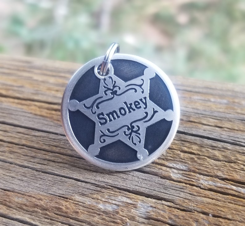 May include: A silver metal dog tag with a black star and the name "Smokey" engraved in the center.