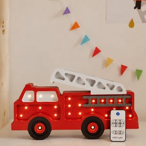 Könnte beinhalten: Eine rote Feuerwehrauto-Lampe aus Holz mit einer weißen Leiter oben, ausgestattet mit integrierten warmen LED-Lichtern in der Kabine, am Körper und in den Rädern. Eine kleine weiße Fernbedienung mit der Aufschrift Little Lights steht davor.