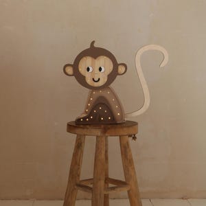 May include: A wooden monkey night light with a brown finish and a smiling face. The light is sitting on a wooden stool.