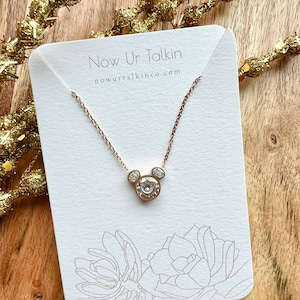 K&ouml;nnte beinhalten: Eine ros&eacute;goldene Halskette mit einem klaren Kristall-Mickey-Mouse-Anh&auml;nger. Die Halskette wird auf einer wei&szlig;en Karte mit dem Text "Now Ur Talkin" und "nowurtalkinco.com" pr&auml;sentiert.