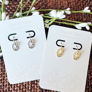 May include: Two pairs of earrings on white cards with the text "Now Ur Talkin" and a website address. One pair is silver and the other is gold.