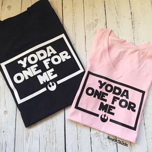 K&ouml;nnte beinhalten: Zwei T-Shirts mit einem schwarz-wei&szlig;en Grafikdesign. Das schwarze T-Shirt hat den Text "YODA ONE FOR ME" in einem wei&szlig;en Kasten. Das rosa T-Shirt hat den gleichen Text in einem schwarzen Kasten.