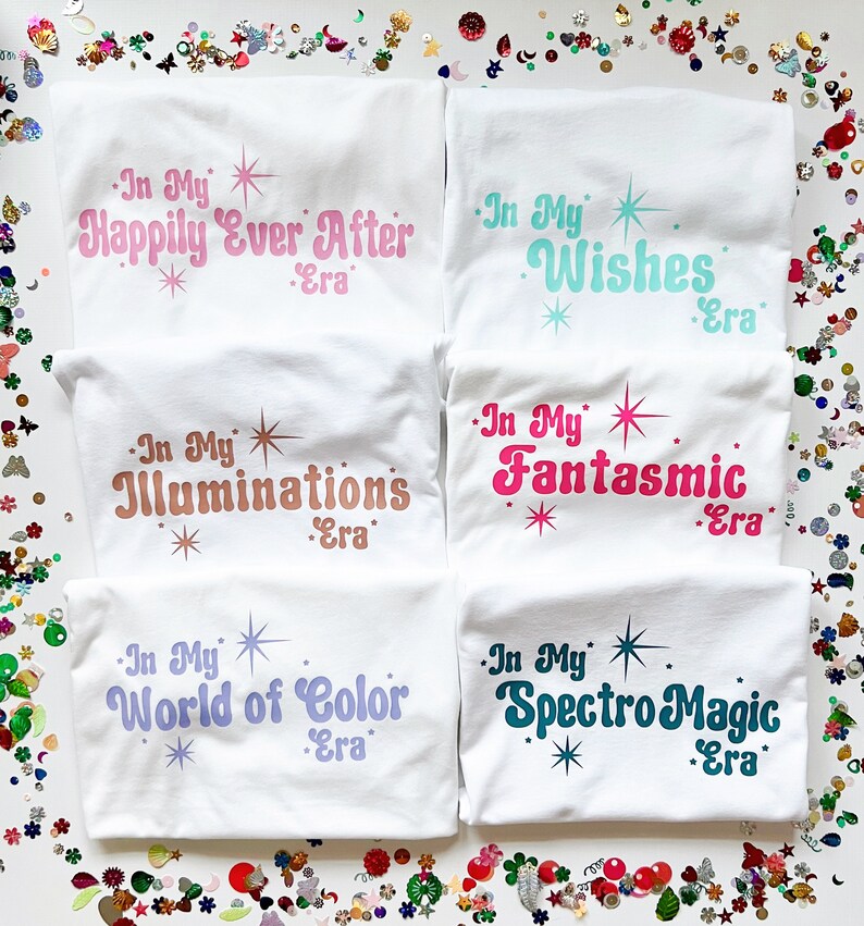 以下が含まれることがあります： カラフルなテキストデザインが施された白いTシャツが5枚。シャツのテキストは「In My Happily Ever After Era」、「In My Wishes Era」、「In My Illuminations Era」、「In My Fantasmic Era」、「In My World of Color Era」です。